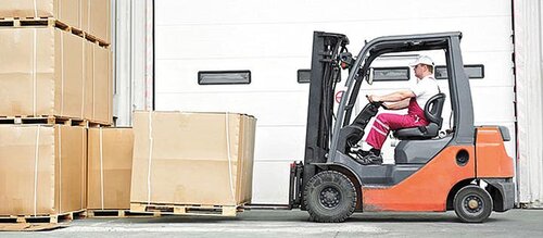 Mann in Gabelstapler fährt Palette mit Paketen hoch