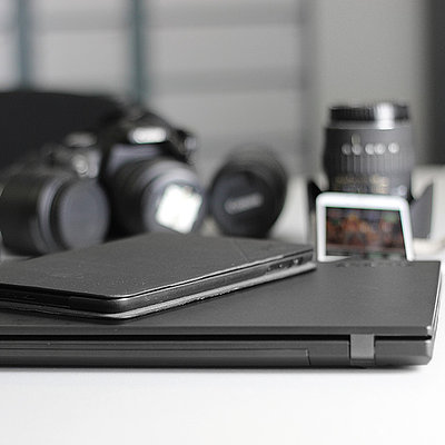 Laptop, Kamera, Smartphone, Fernglas und Tablet auf Tisch liegend