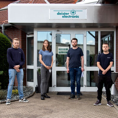 Vier Auszubildende stehen vor dem Eingang von deister electronic