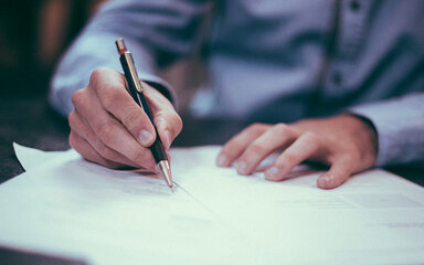 Person die mit einem Stift auf einem Zettel schreibt