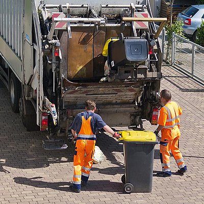 Müllwagen in den eine Tonne entleert wird und Müllmänner davorstehend