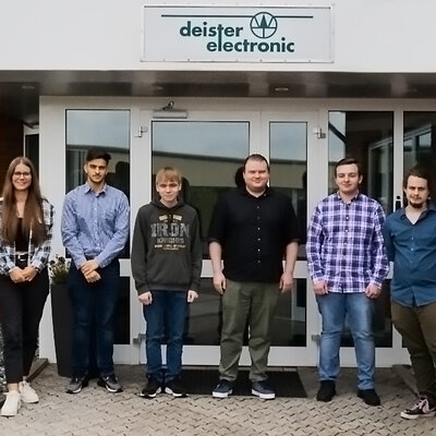 Fünf Auszubildende stehen vor dem Eingang von deister electronic